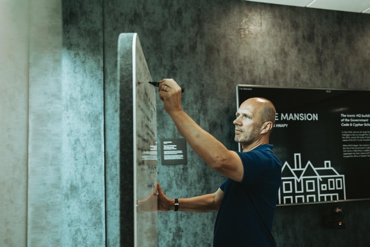 A man in a blue shirt writing on a whiteboard