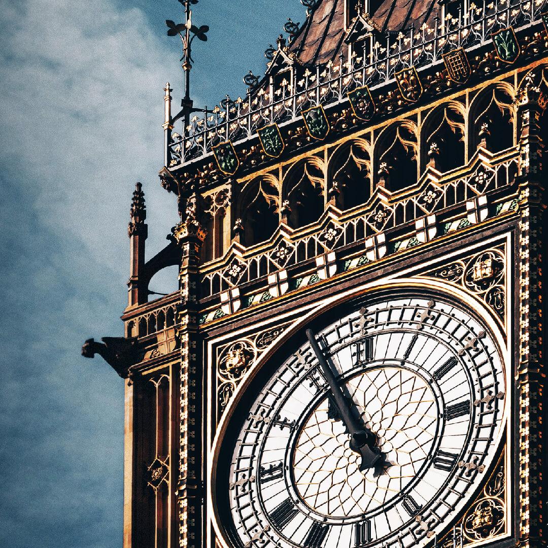 Close-up of the ornate clock face of Big Ben, featuring Roman numerals and intricate architectural details against a cloudy sky.