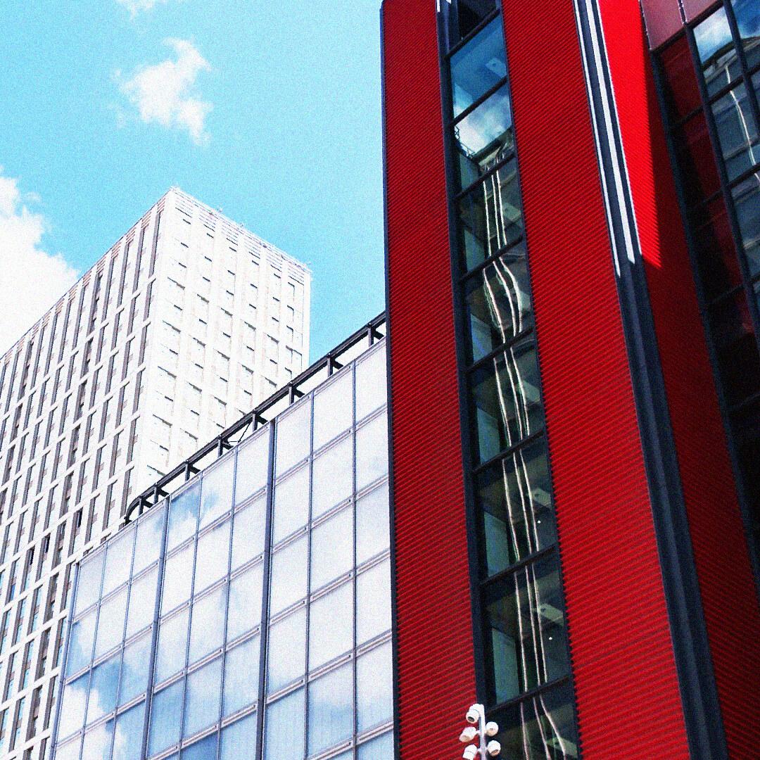 Modern buildings with red and glass facades under a blue sky with clouds.