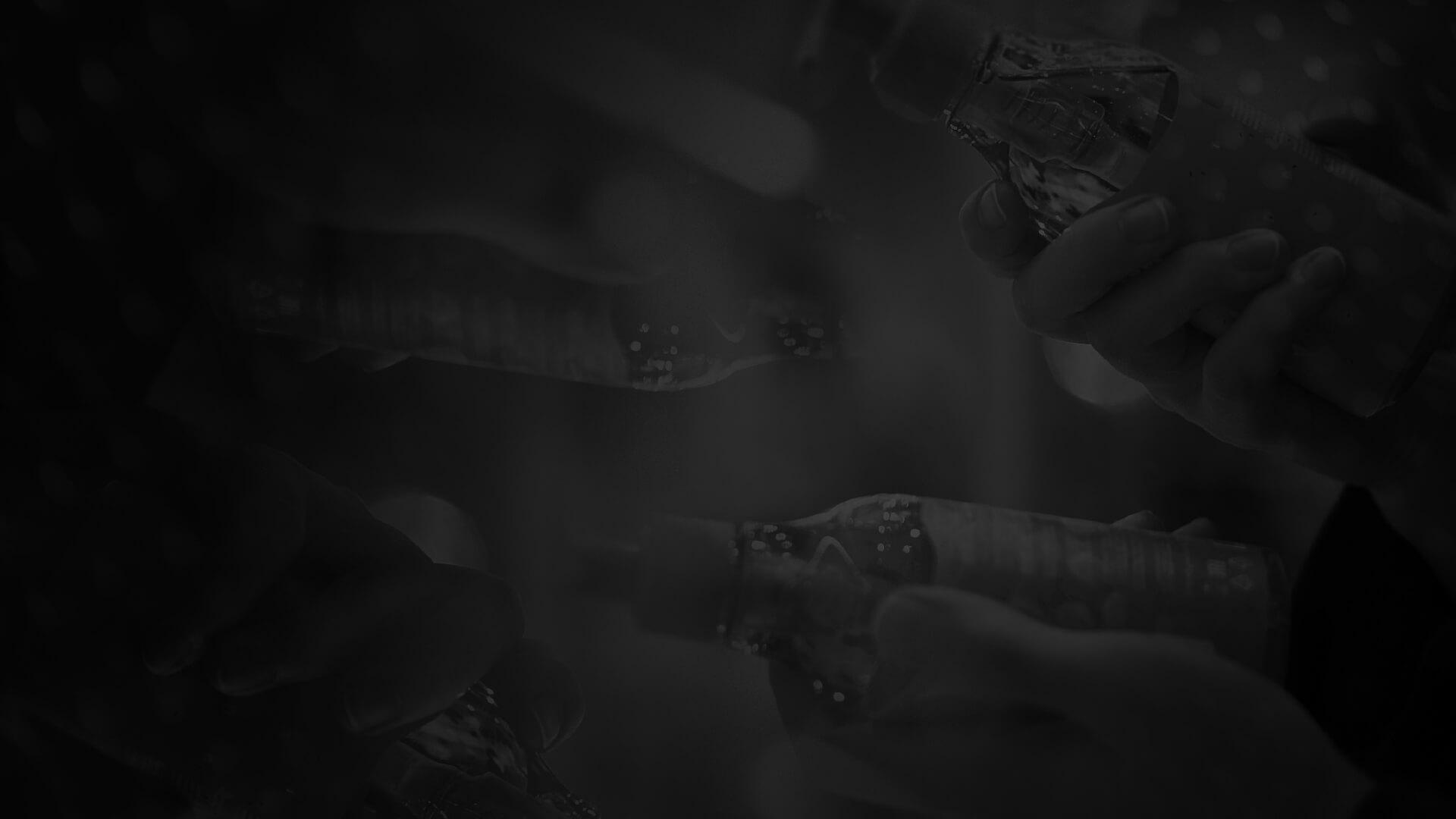 Hands holding patterned bottles in a dark, reflective scene, creating a symmetrical and abstract visual effect.